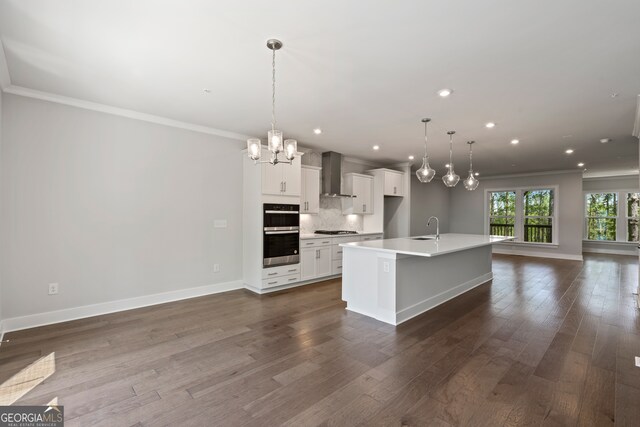 kitchen with a kitchen island with sink, sink, white cabinets, wall chimney range hood, and stainless steel appliances