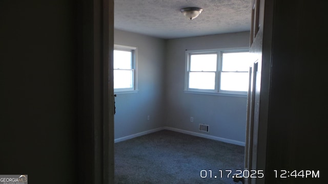 unfurnished room with a textured ceiling and dark carpet