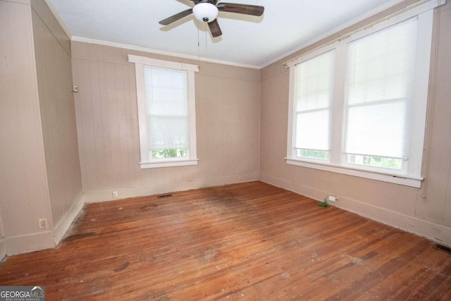 spare room with ceiling fan, wood walls, crown molding, and hardwood / wood-style floors