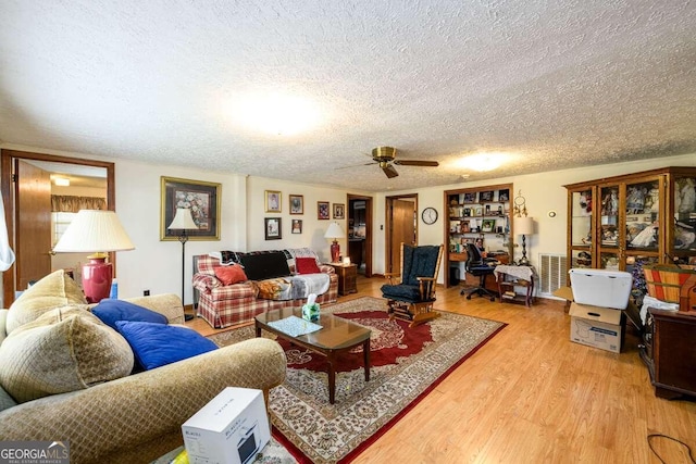 living room with a textured ceiling, ceiling fan, and light hardwood / wood-style flooring