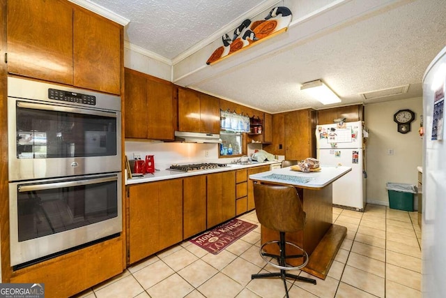 kitchen featuring light tile patterned flooring, a kitchen island, a textured ceiling, appliances with stainless steel finishes, and crown molding