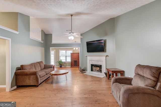 living room featuring a premium fireplace, light hardwood / wood-style floors, ceiling fan, and a textured ceiling