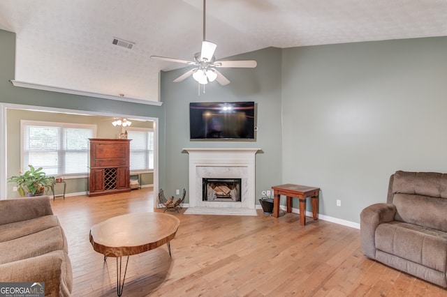 living room featuring light hardwood / wood-style flooring, vaulted ceiling, a premium fireplace, and a textured ceiling