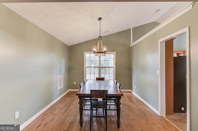 dining area with light hardwood / wood-style floors, vaulted ceiling, and an inviting chandelier