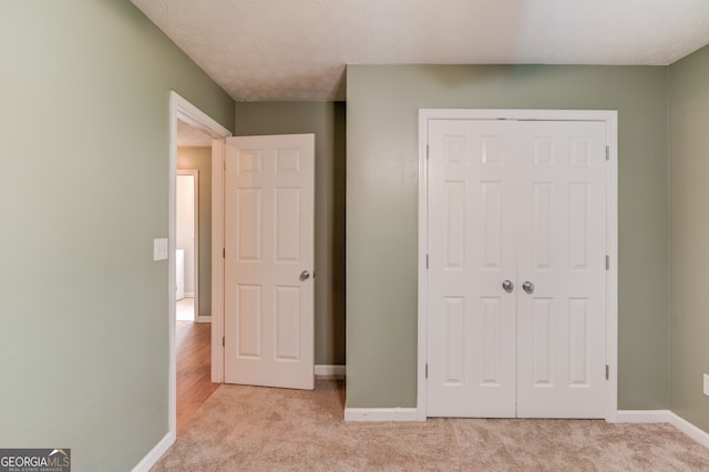 unfurnished bedroom featuring light carpet, a textured ceiling, and a closet