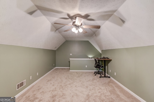 unfurnished office featuring a textured ceiling, vaulted ceiling, ceiling fan, and light colored carpet