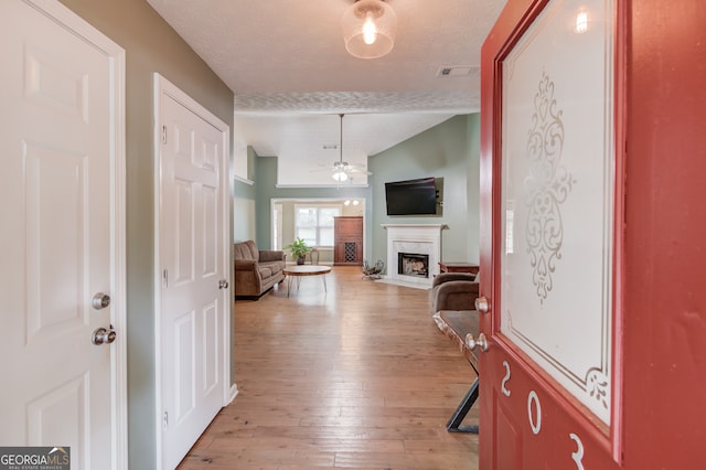 foyer with ceiling fan, light hardwood / wood-style floors, a fireplace, and a textured ceiling