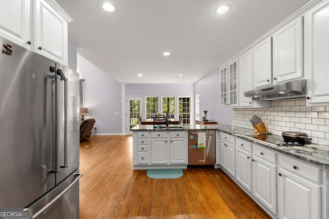 kitchen with white cabinets, kitchen peninsula, dark stone counters, stainless steel appliances, and light wood-type flooring