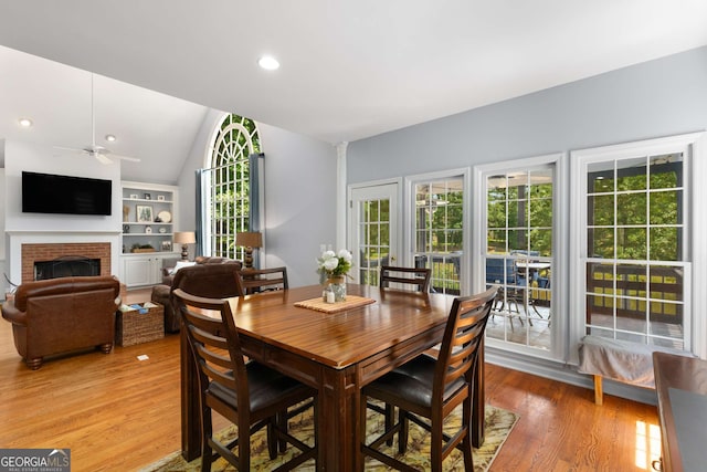 dining room featuring lofted ceiling, ceiling fan, hardwood / wood-style flooring, and a fireplace