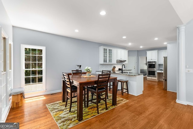 dining space featuring sink, light hardwood / wood-style flooring, and ornate columns