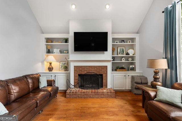 living room with light wood-type flooring, vaulted ceiling, and a brick fireplace