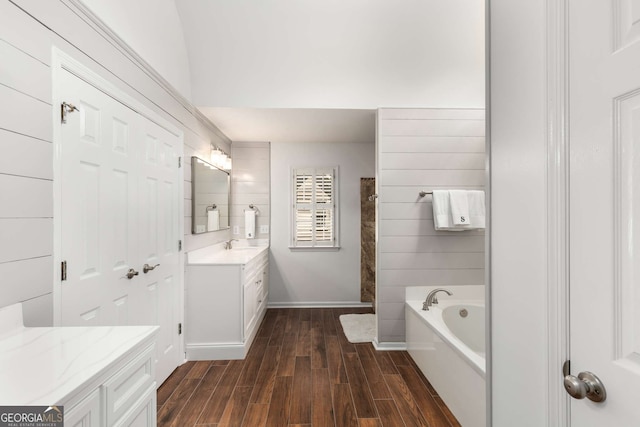 bathroom with wood-type flooring, vanity, vaulted ceiling, and a washtub