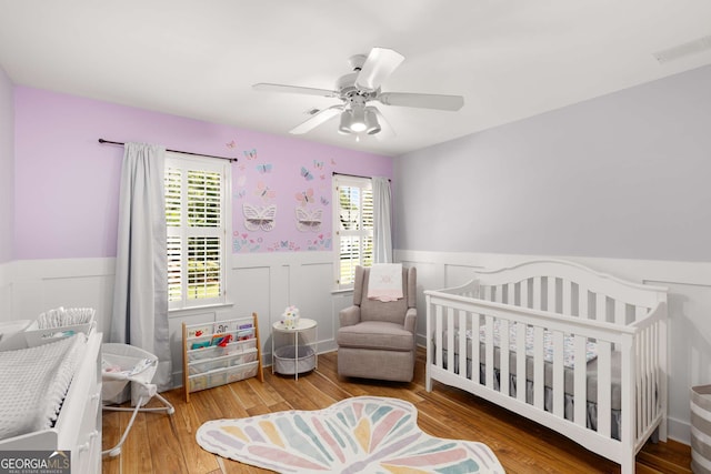 bedroom featuring a crib, wood-type flooring, and ceiling fan