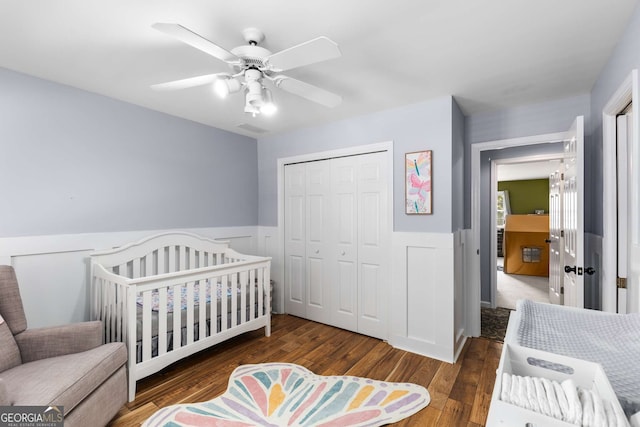 bedroom with a closet, ceiling fan, a crib, and dark hardwood / wood-style floors