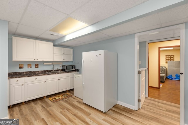 kitchen featuring light wood-type flooring, white refrigerator, sink, white cabinetry, and a paneled ceiling