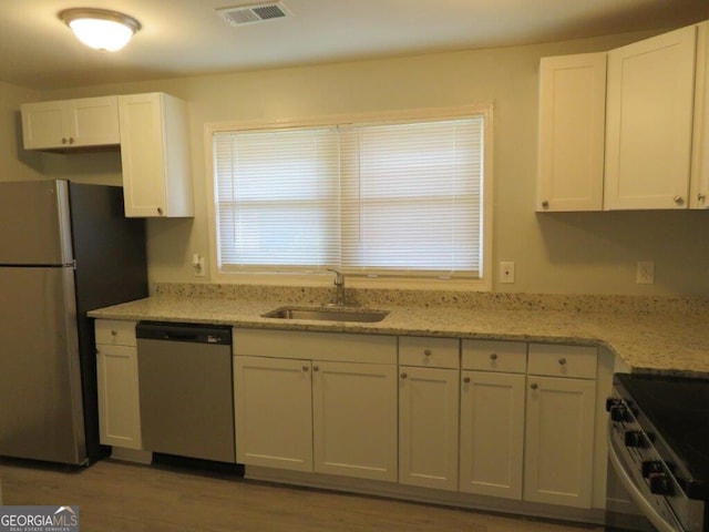 kitchen with light wood-type flooring, light stone counters, sink, white cabinetry, and stainless steel appliances