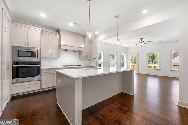 kitchen featuring pendant lighting, a kitchen island with sink, dark wood-type flooring, appliances with stainless steel finishes, and custom range hood