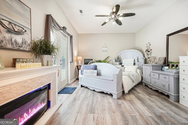 bedroom featuring ceiling fan, a stone fireplace, a textured ceiling, and light wood-type flooring