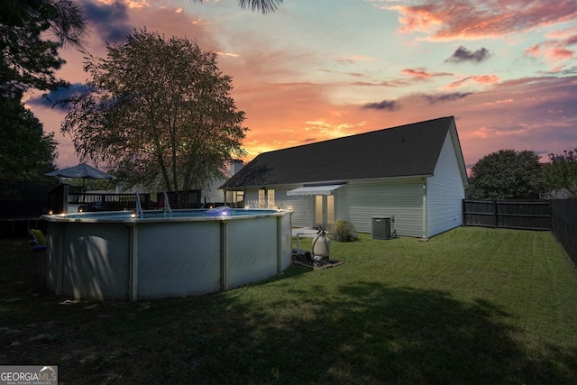 yard at dusk featuring central AC and a fenced in pool