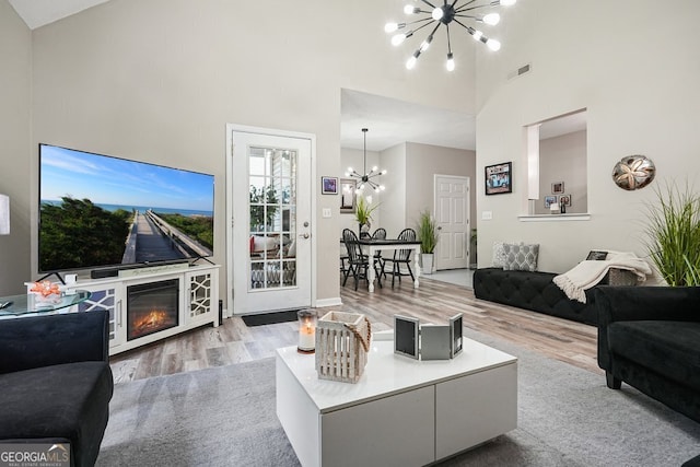 living room with a chandelier, high vaulted ceiling, and light wood-type flooring