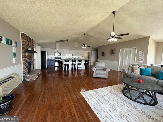 living room featuring ceiling fan, a wall mounted air conditioner, dark hardwood / wood-style flooring, vaulted ceiling, and a fireplace