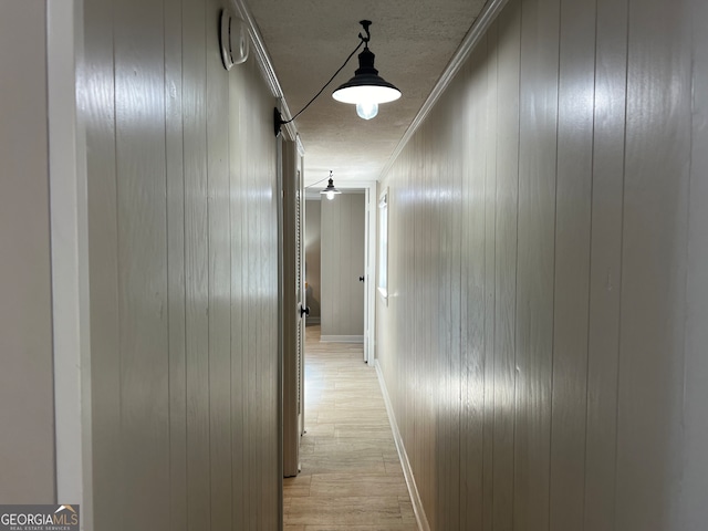 hall with wood walls, light wood-type flooring, and ornamental molding