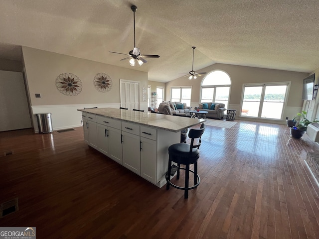 kitchen with white cabinets, a center island, dark hardwood / wood-style flooring, and light stone countertops