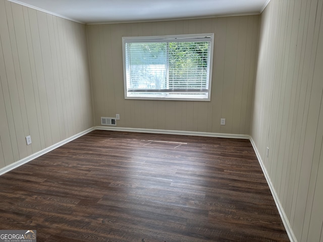 empty room featuring wood walls, ornamental molding, and dark hardwood / wood-style flooring