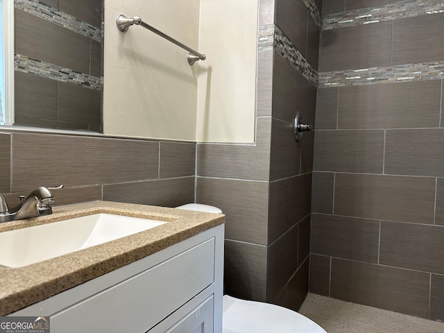 bathroom featuring tile walls, tiled shower, vanity, and toilet