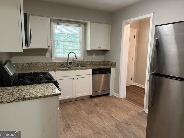 kitchen with appliances with stainless steel finishes, dark stone countertops, white cabinets, light wood-type flooring, and sink