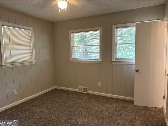 carpeted spare room featuring a textured ceiling, wood walls, and ceiling fan