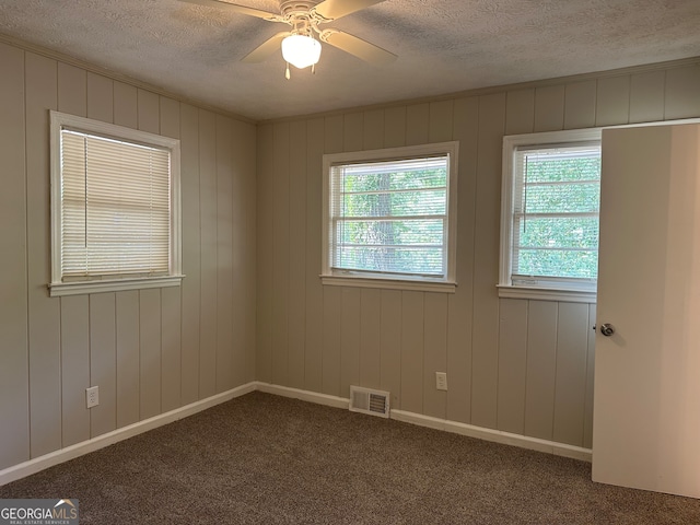 carpeted spare room with wood walls, ceiling fan, and plenty of natural light