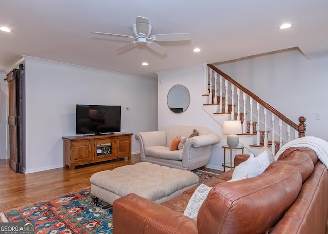 living room with a barn door, wood-type flooring, crown molding, and ceiling fan