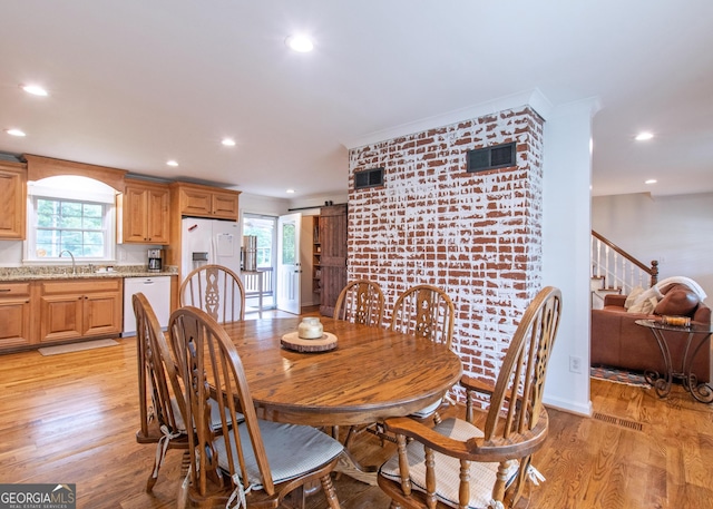 dining area featuring ornamental molding, light wood-type flooring, sink, and a barn door