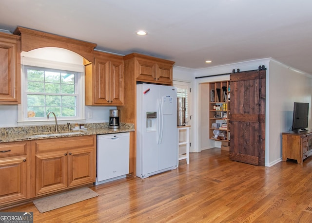 kitchen with light stone counters, sink, white appliances, light wood-type flooring, and a barn door