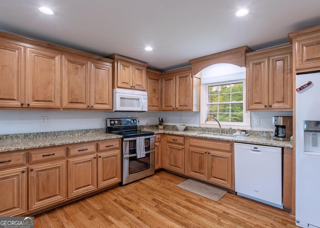 kitchen with light stone countertops, light hardwood / wood-style flooring, sink, and white appliances