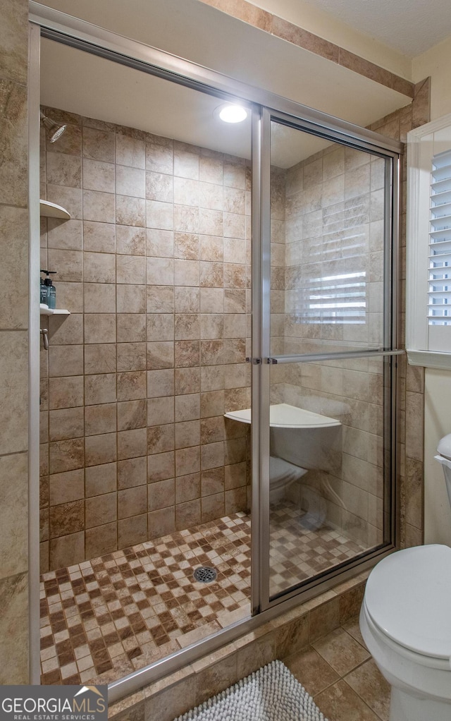 bathroom with tile patterned flooring, toilet, and a shower with shower door