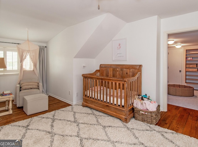 bedroom with wood-type flooring, a nursery area, and lofted ceiling