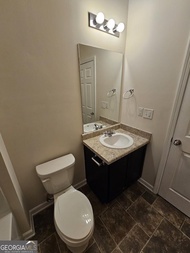 bathroom featuring stone finish flooring, baseboards, toilet, and vanity