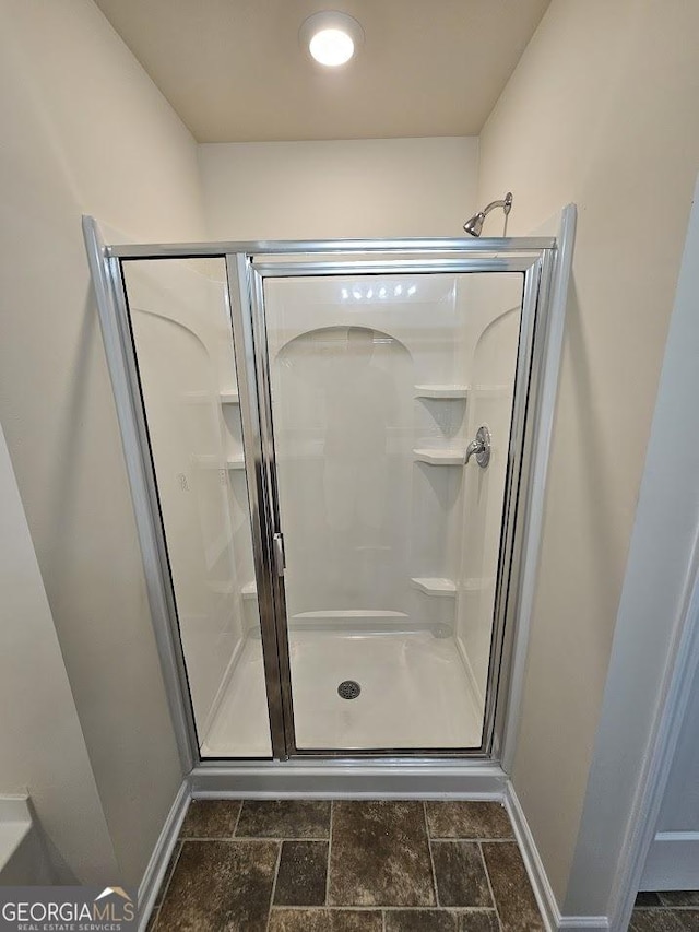 bathroom with stone finish flooring, baseboards, and a shower stall