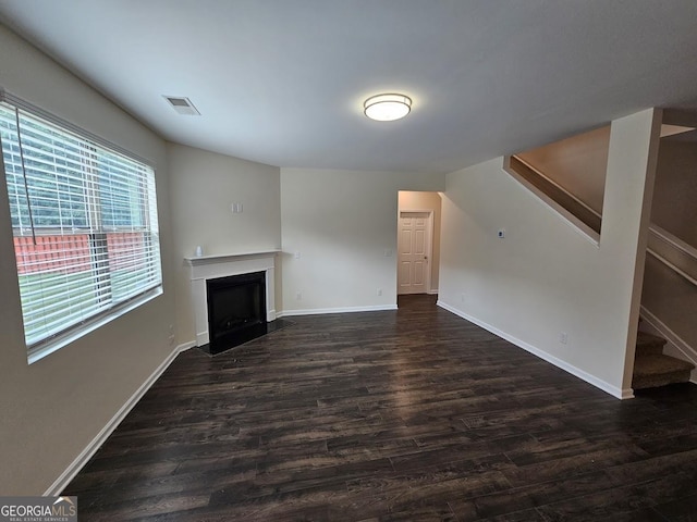 unfurnished living room featuring dark wood-style floors, baseboards, visible vents, a fireplace, and stairs