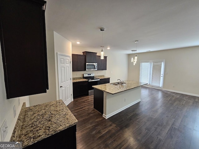 kitchen featuring pendant lighting, a center island with sink, a sink, dark wood finished floors, and appliances with stainless steel finishes