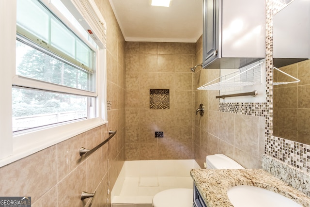 bathroom with tile walls, tiled shower, vanity, and toilet