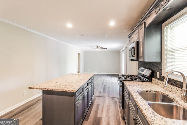 kitchen with light wood-type flooring, light stone counters, sink, a kitchen island, and appliances with stainless steel finishes