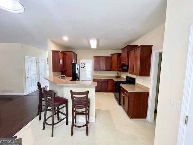 kitchen with black appliances, sink, light hardwood / wood-style flooring, and a breakfast bar