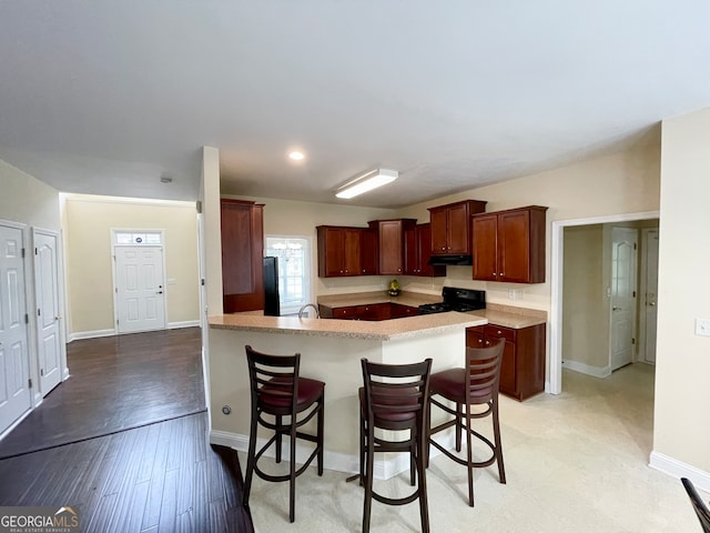 kitchen with light wood-type flooring, black appliances, sink, and a breakfast bar