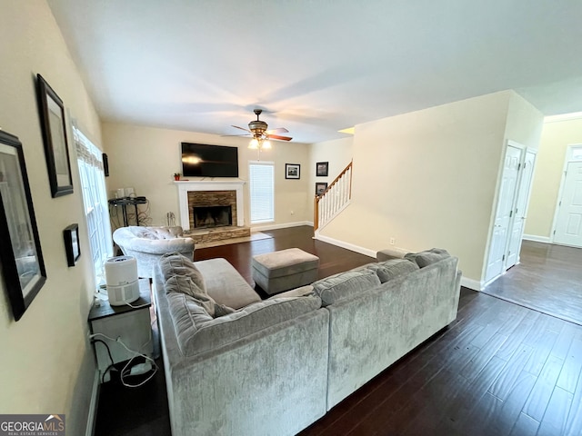 living room with ceiling fan, a stone fireplace, and dark wood-type flooring