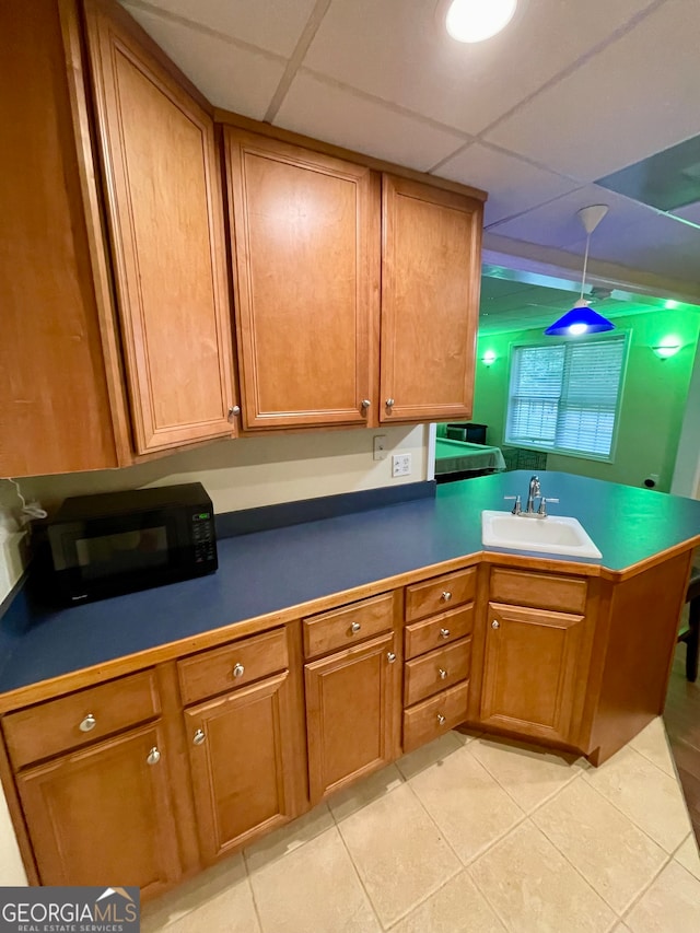 kitchen featuring sink, kitchen peninsula, a paneled ceiling, decorative light fixtures, and light tile patterned floors