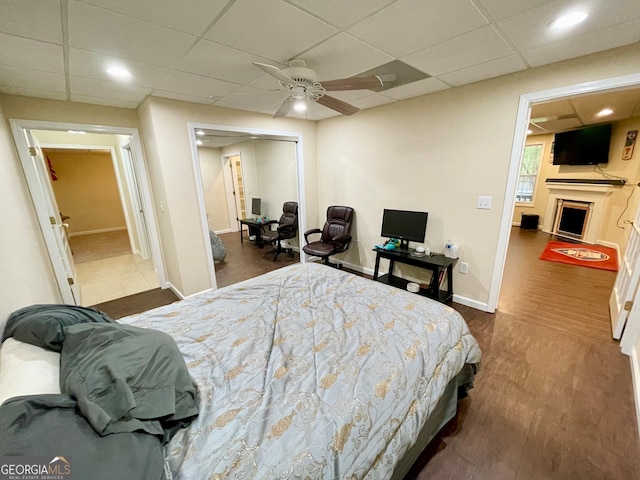 bedroom with ceiling fan, a drop ceiling, and dark wood-type flooring