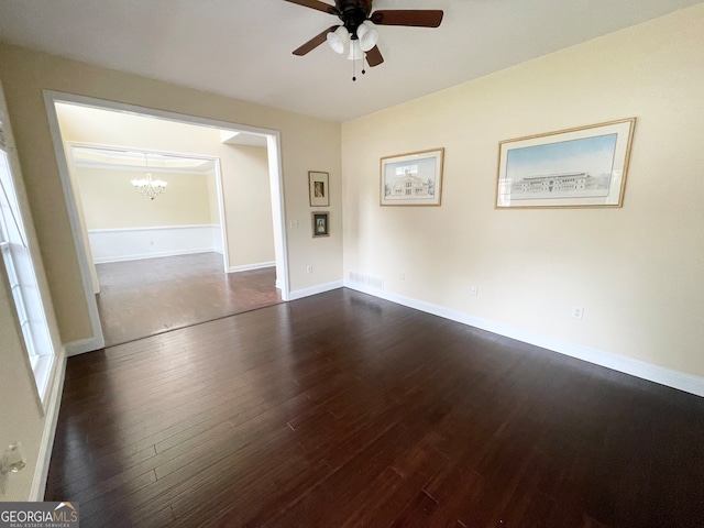 spare room with ceiling fan with notable chandelier and dark wood-type flooring